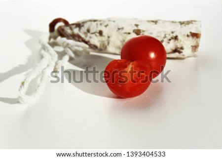 Traditional Spanish Fuet thin dried sausage with cherry tomatoes on white background