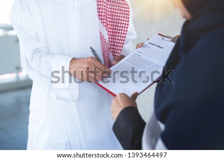Arab secretary holds documents to manager to sign, Arab man signing documents  Royalty-Free Stock Photo #1393464497