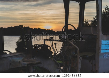 Old tractor with sun setting in the background over a river