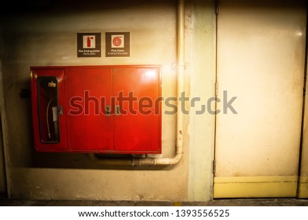 Fire extinguisher and red fire hose reel in hotel corridor and fire exit door