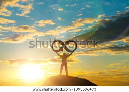 A silhouette of a man holds an infinity symbol on top of a mountain with a sunset background. Concept idea, life, success, business.