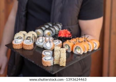 A stylish young smiling girl poses for a photo and holding in her hand a plate of rolls and chopsticks in the other hand. Appetizing advertising photography for restaurant, sushi bar, delivery