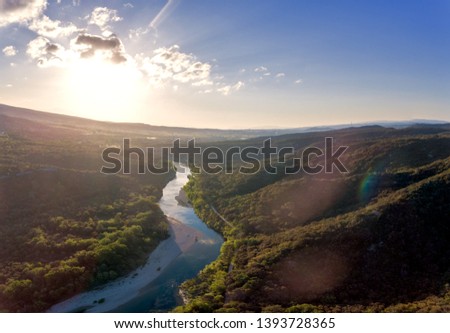 Stunning aerial drone shot of the Rhone river at sunrise. The river reflects the early morning sun and the river gorge is forested and green. An old roman bridge can be see in the distance. Royalty-Free Stock Photo #1393728365