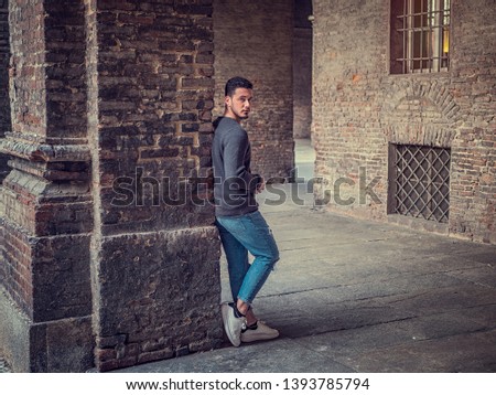 Attractive young man standing against old brick wall in European city, looking at camera.