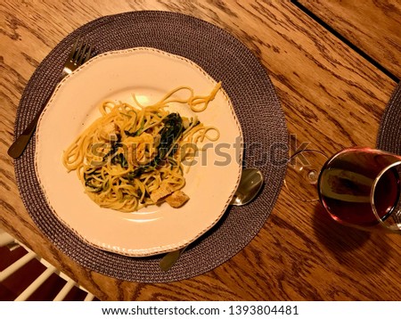 Homemade Spaghetti with Baby Spinach and Chicken at Dinner Table with Glass of Wine.