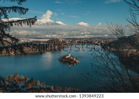 Photo of Lake Bled in Slovenia. Church in the middle of lake's island. Water reflections, trees covered in snow