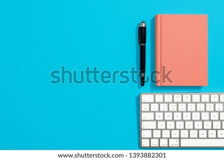 Orange hardcover notebook with black pen on a pastel blue background with a computer keyboard.  Right side composition with copy space and room for text