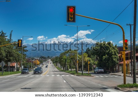 Daytime image of a street or avenue, with traffic lights, some cars and the snowy mountains Royalty-Free Stock Photo #1393912343