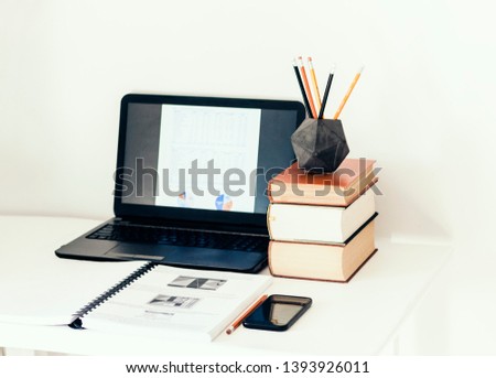 Laptop, stack of books, smartphone, notebook and pencils in concrete holder on white table in office business background for education learning concept