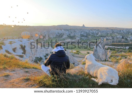 The photo was taken in Turkey, in the sisterhood called Cappadocia. In the picture, a young boy and his friend the dog are watching the balloons take off at dawn.