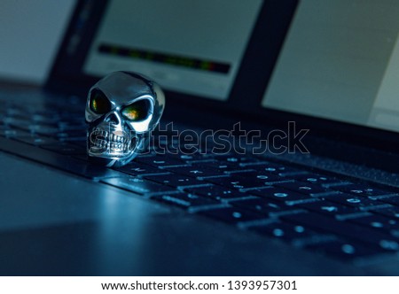 A skull made of shiny metal lies on a keyboard of a computer in dark atmosphere.
