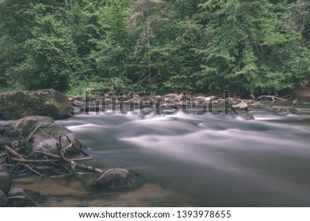 long exposure rocky mountain river in summer with high water stream level in forest with trees and sandy foreground shore - vintage old film look