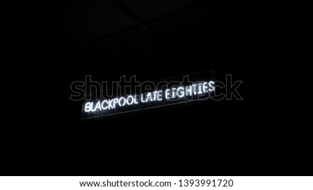 Bright fluorescent white neon sign that says : 'BLACKPOOL LATE EIGHTIES'. The neon sign is surrounded by black darkness, a great centrepiece for any establishment.