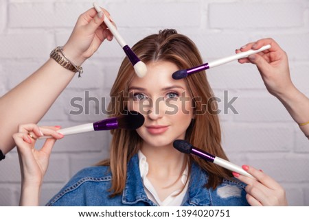 Studio photo of many hands with brushes doing make-up process to young caucasian beautiful woman on white background. Concept with many hands, lady is having a procedure of applying make-up