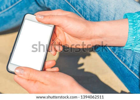 Image Mockup of beautiful hands of a woman holding a white mobile phone with a blank screen on her hip on the beach, on the sand. Close up.
