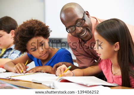 Teacher Helping Pupils Studying At Desks In Classroom Royalty-Free Stock Photo #139406252