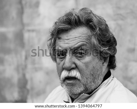 Black and white portrait of a middle aged caucasian man with gray hair, a mustache and a beard on a gray background
