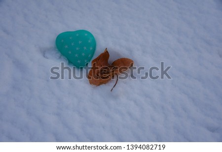 Two gold wedding rings sitting inside a autumnal colored leaf next to a heart shaped green stone on top of a fresh snow background. Copy space.