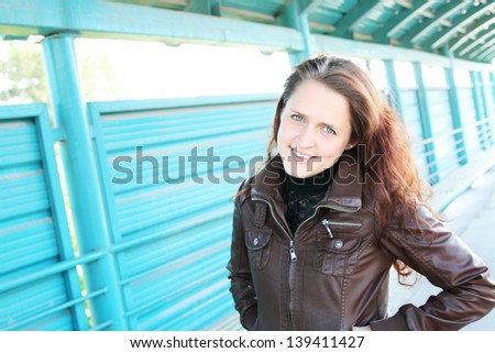 A young girl with ginger hair posing by a fence on a nice autumn afternoon.