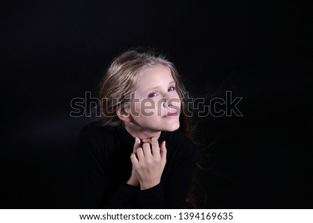 Portrait of a blonde girl with long hair on a black background. Emotional portrait.The girl shows different emotions on the face. Plays with long hair.Child portrait concept.