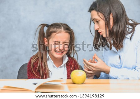 Mom talking to her baby. During this on a gray background. The girl cries, mom stroking her hand and talking to her daughter. Gray background. On the desk of the book and a green apple.