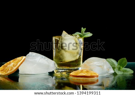 Chilled alcoholic cocktail with ice orange and fresh herbs on black background