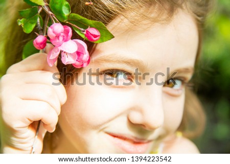 joyful little girl put a branch of a blossoming cherry tree on her head on a sunny day, a sly look