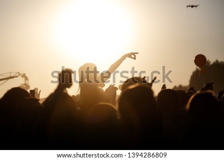 The crowd enjoys the summer music festival, sunset, the black silhouettes hands up, girl in the center