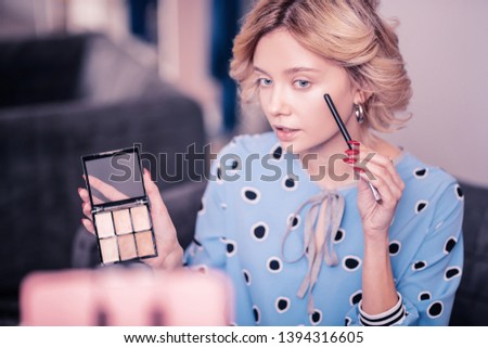 Telling some secrets. Blue-eyed beauty blogger wearing spotted dress telling some secrets about concealer
