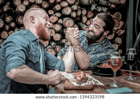 Situation is heating up. Portrait of two friends fighting in an all-out arm-wrestling battle after drinking a couple of beer glasses.