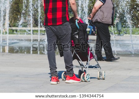 Lonely single father hipster in checkered red and black shirt with a stroller walking in the city park.