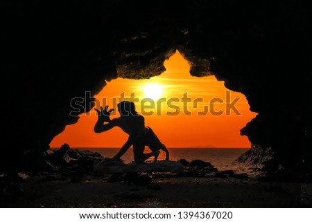 Caveman posture or action in the cave at red sky sunset background