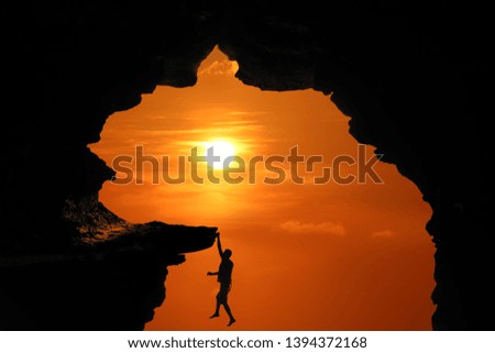 Silhouette of Man climbing in the cave or high cliffs at a red sky sunset background.
