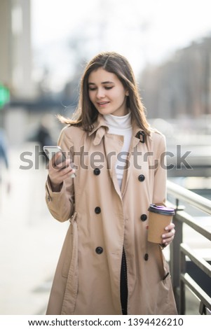Pretty girl stand on the street use phone and drink coffee
