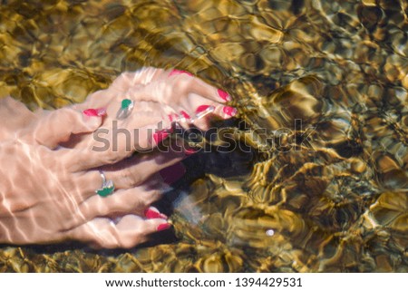 Closeup hands of a young woman with red manicure on nails under water with copy space.