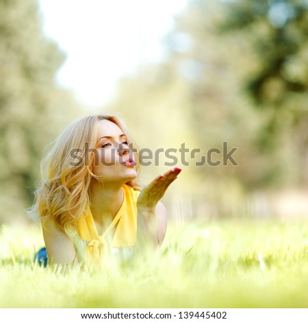 Happy young woman lying on grass and blowing kiss