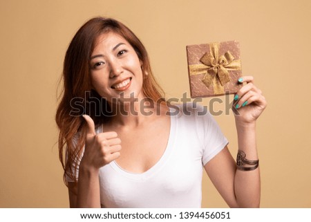 Young Asian woman thumbs up with a gift box on beige background
