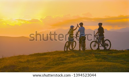COPY SPACE Three young friends celebrate a successful cross country bike trip on a sunny summer evening in idyllic Slovenian mountains. Tourists ride bicycles up to edge of a grassy hill and high five Royalty-Free Stock Photo #1394523044