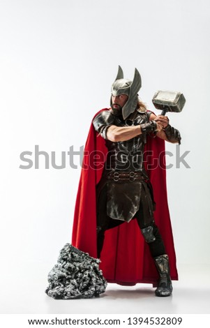 Long hair and muscular male model in leather viking's costume with the big hammer cosplaying isolated on white studio background. Full-lenght portrait. Fantasy warrior, antique battle concept.