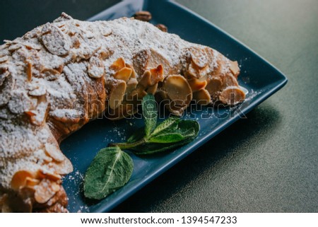 Tasty croissant with powdered sugar and mint on the plate on a dark background