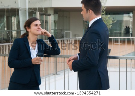 Relaxed business woman and man chatting outdoors. Colleagues talking with railing and building glass wall in background. Break and communication concept. Side view.