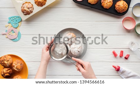 partial view of woman decorating cupcakes with powdered sugar on table with baking tools