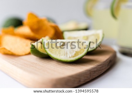 Fresh avocado, lime, drink and nacho chips lying on marble background. Recipe for Cinco de Mayo party
