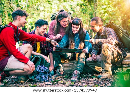 Group of happy friends on outdoors outfit looking at map sitting  in the
 forest - Active teenagers on excursion day planning trekking route - Concept of teamwork , friendship and hike - Image