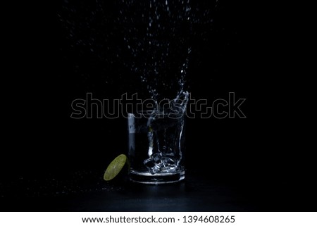 water splash with ice cubes and lemon in a glass on black background.