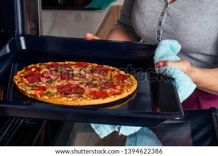 woman openung ovens and take pizza with tomatoes, olives, mushrooms and cheese sausage