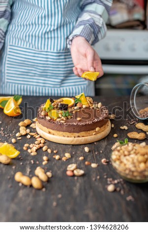 Confectioner decorates chocolate cake with orange and mint leaves with peanuts and nuts. Healthy raw gluten-free and milk-and flour-free desserts for vegan food