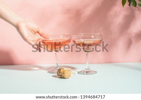 Female hand elegantly holding a glass of champagne or wine delicate pink background bright sunlight. Concept minimalism.