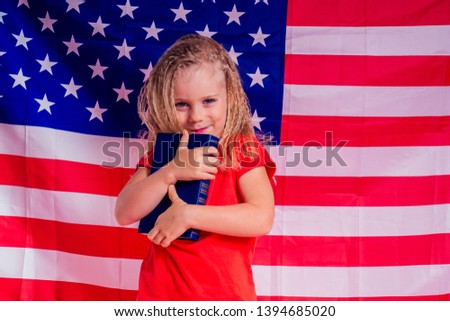 Little Blue eyes blonde charming girl holding an encyclopedia book alphabet foreign language against american flag background. independence day usa 4th of July 