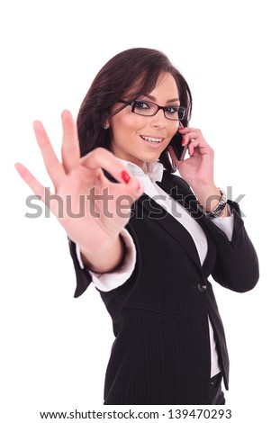 young business woman shows the ok sign while on the phone, smiling at the camera. on white background
